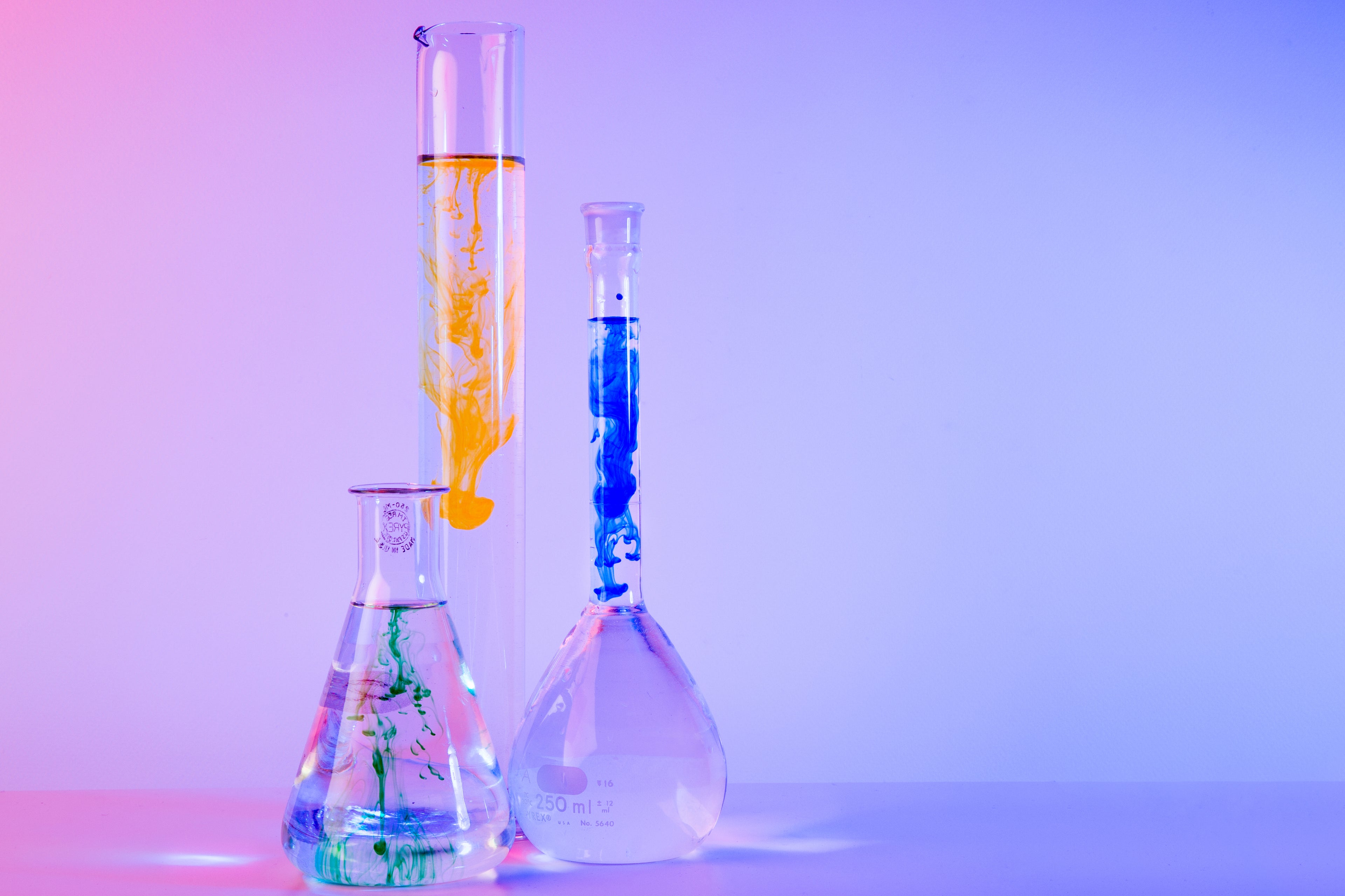 Colorful liquids diffusing in laboratory glassware under pink and blue lighting
