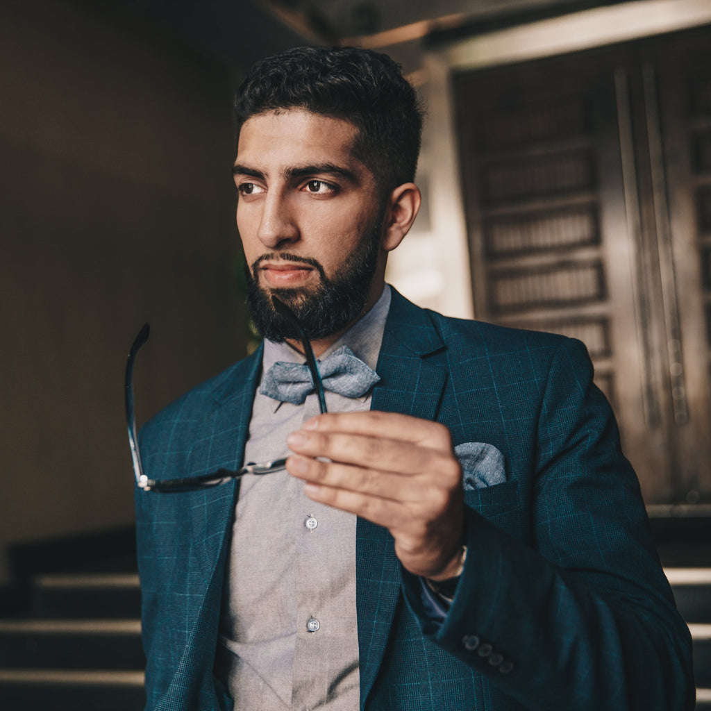 Man in a blue suit holding eyeglasses and looking thoughtfully ahead
