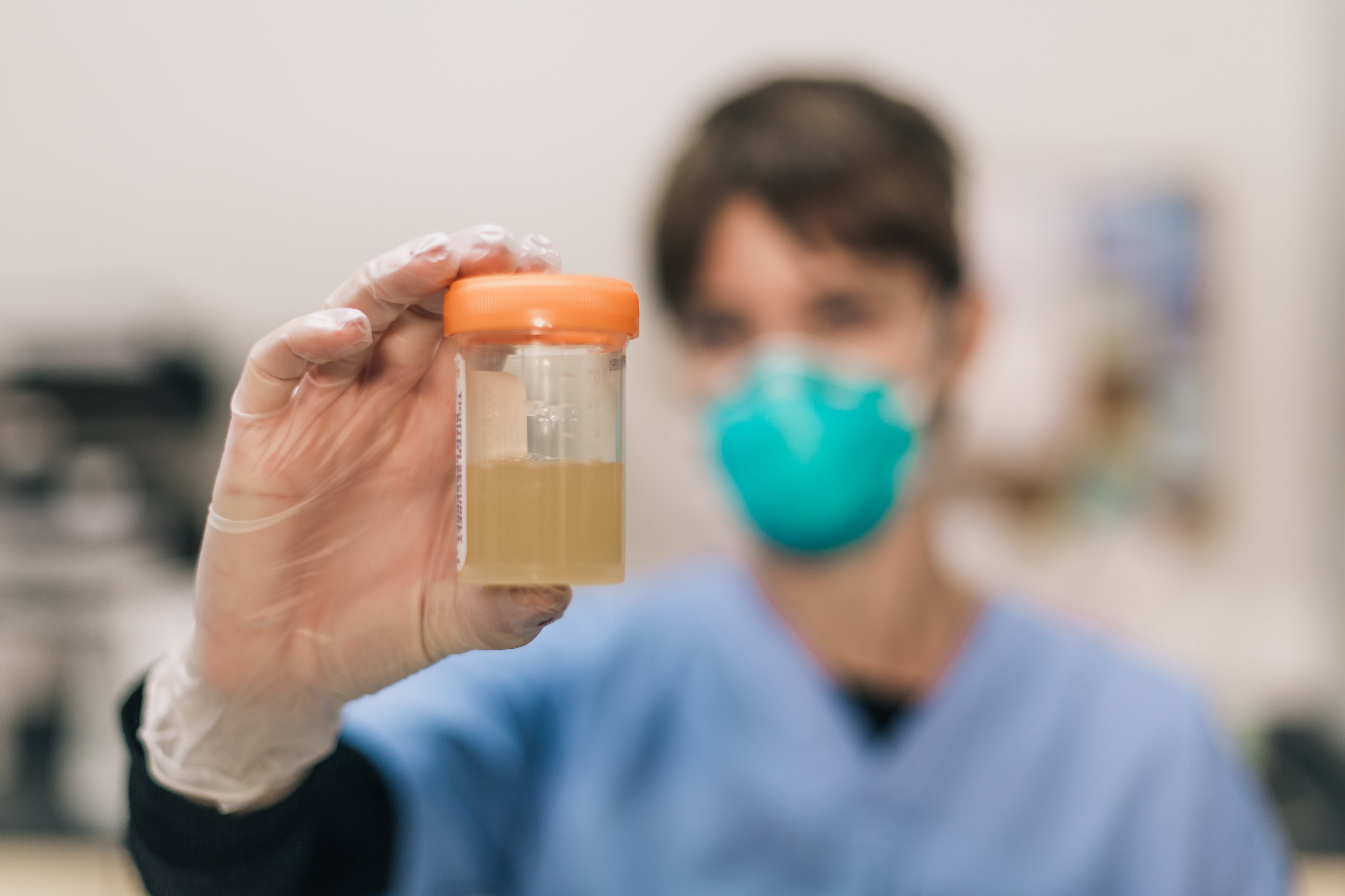 Medical professional wearing gloves and mask displaying sample jar